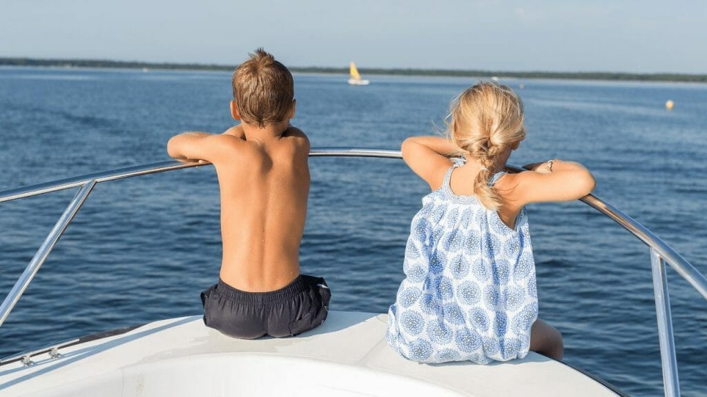A girl and a boy on a boat staring at the sea.