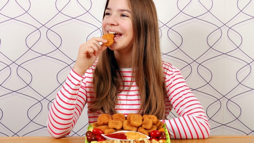 Teenage girl eats chicken nuggets and applies mindful eating techniques.