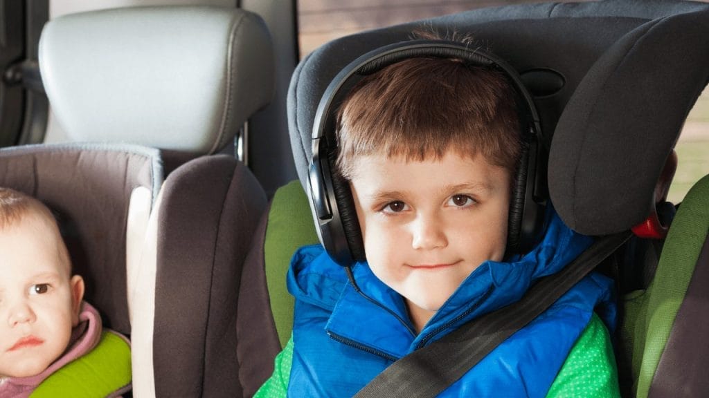 A young boy wearing headphones in the backseat of the car.