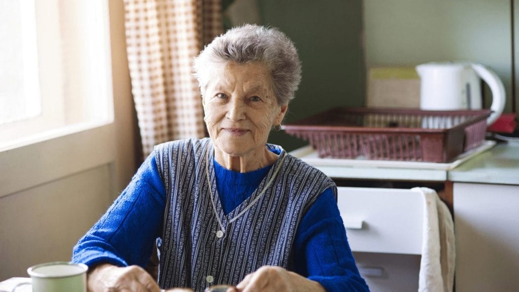 Elderly woman sits on the kitcen table and smiles